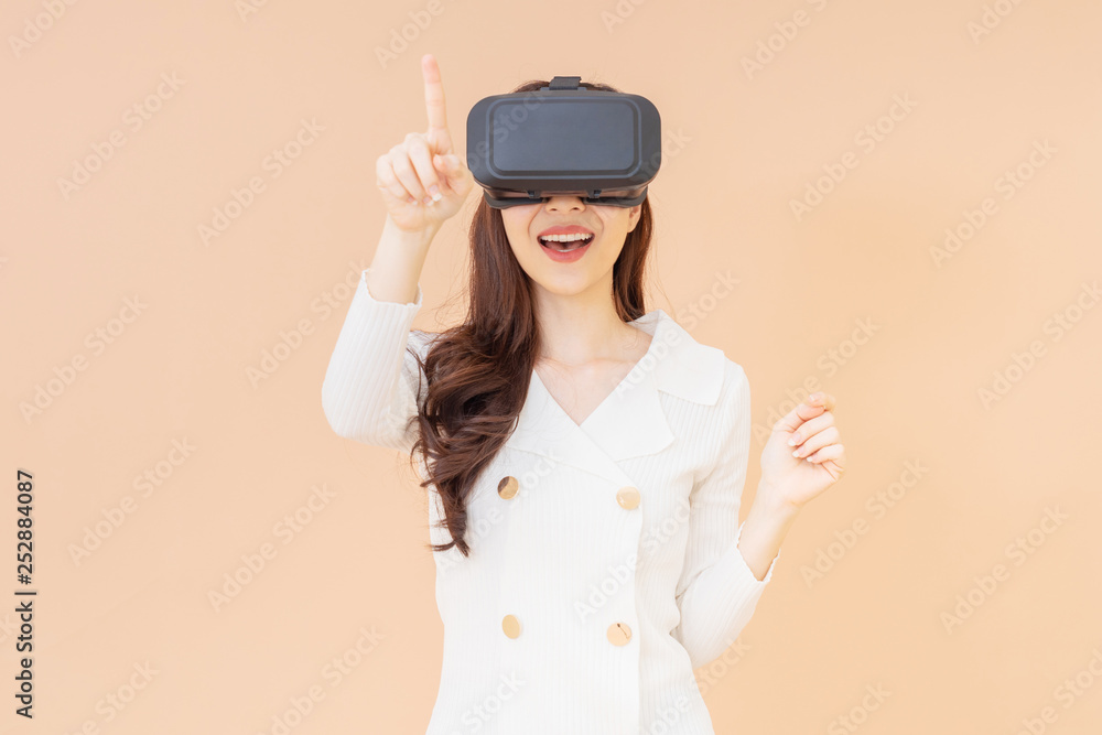portrait of a young asia woman wearing a white cardigan and VR glasses. She is amazed by what she is seeing. Virtual reality headset. isolated orange background portrait of a young asia woman wearing a white cardigan and VR glasses. She is amazed by what she is seeing. Virtual reality headset. isolated orange background