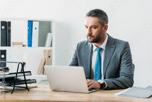 concentrated and focused advisor in suit using laptop at wokspace photo