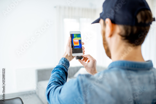 Man checking the house heat loss and the temperature of radiator with thermovision camera and smart phone in the house