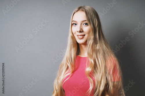 happy smiling young woman with long blond hair and pink t-shirt against gray background with copy space