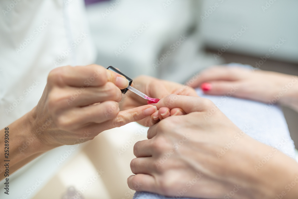 Closeup of manicurist applying shiny red nail polish