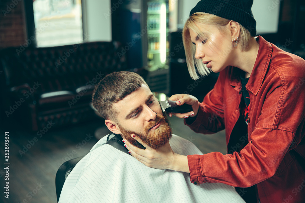 Client during beard shaving in barbershop. Female barber at salon. Gender equality. Woman in the male profession. Client during beard shaving in barbershop. Female barber at salon. Gender equality. Woman in the male profession.