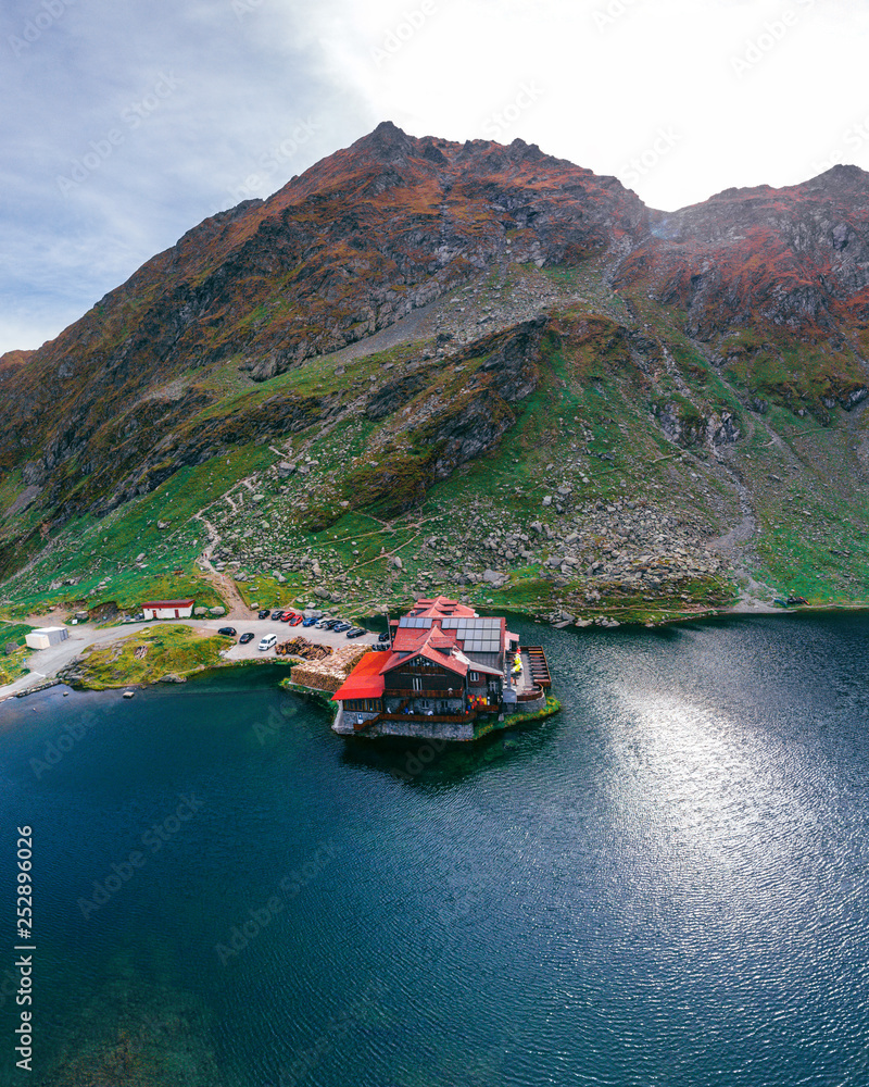 Aerial view on house, hotel on the shore of a mountain lake, Balea Lac, Romania, large panorama, tourism and vacation concept, travel and active lifestyle, vertical photo