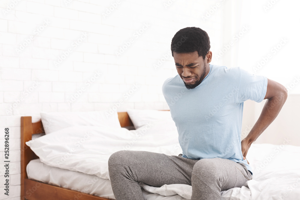 Man suffering from back pain at home in bedroom. Man suffering from back pain at home in bedroom.