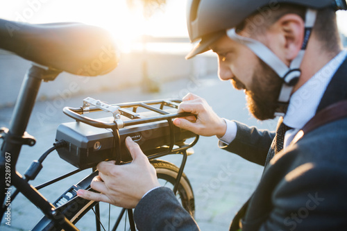 Hipster businessman commuter setting up electric bicycle in city.