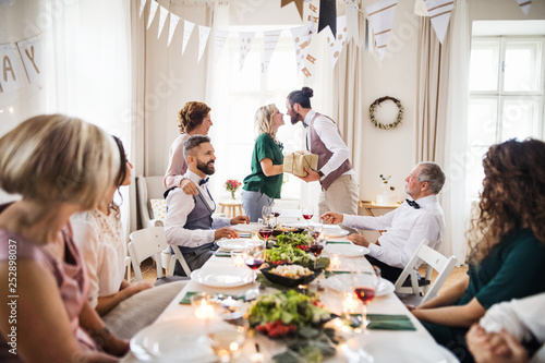 A man giving gift to a young surprised woman on a family birthday party.