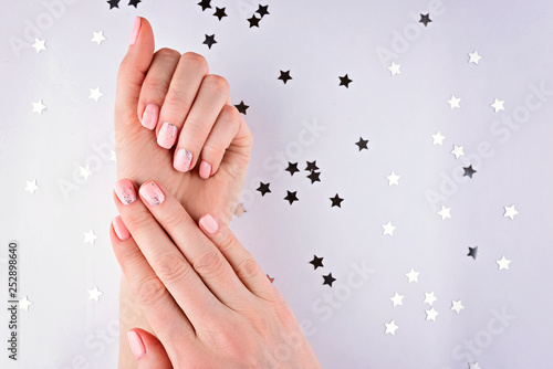 Woman's hands with a pink manicure on a white background with silver stars. Confetti.