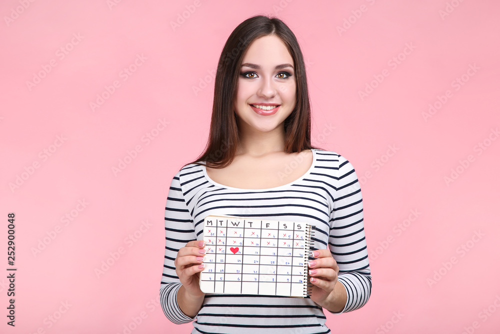 Beautiful young woman with calendar on pink background Beautiful young woman with calendar on pink background