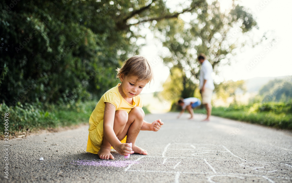 Small cute girl on a road in countryside in sunny summer nature, drawing with chalk. Small cute girl on a road in countryside in sunny summer nature, drawing with chalk.