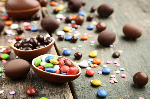 Chocolate easter eggs with colorful candies on grey wooden table