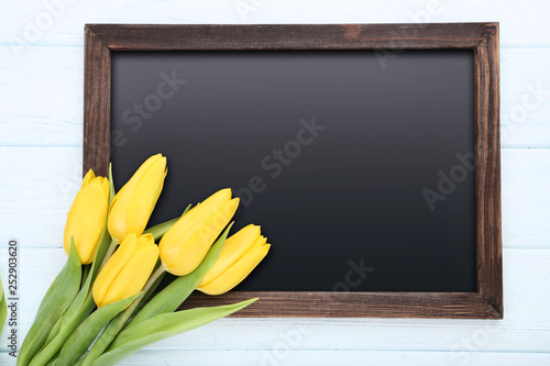 Bouquet of yellow tulips with blank frame on wooden table