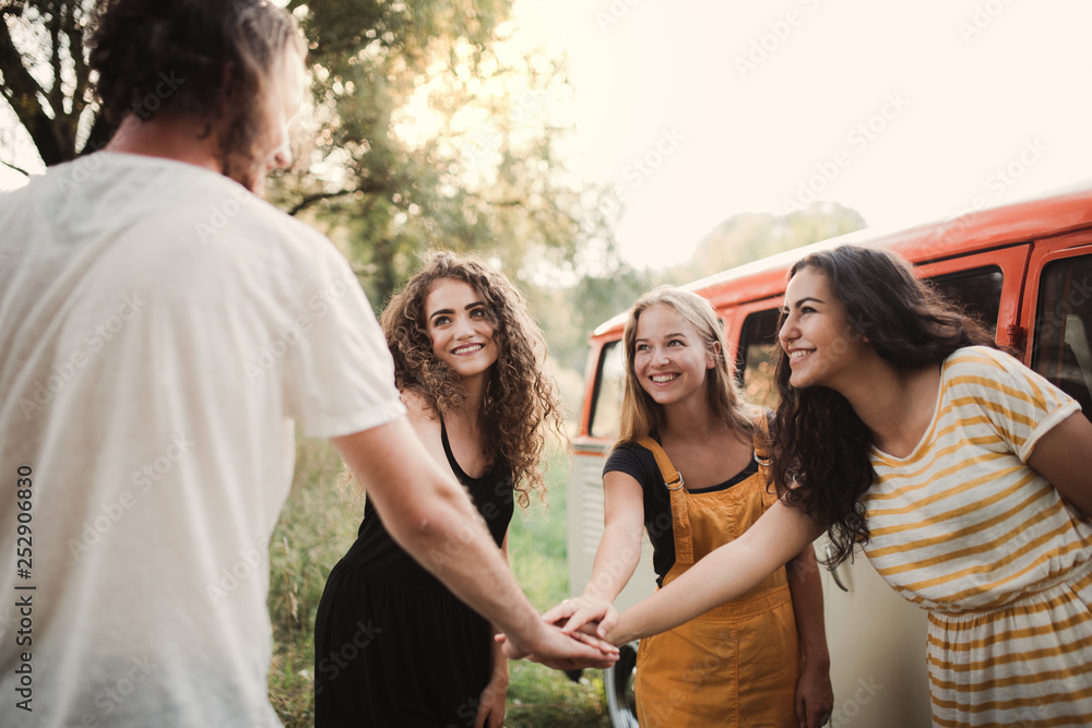 A group of young friends on a roadtrip through countryside, putting hands together.