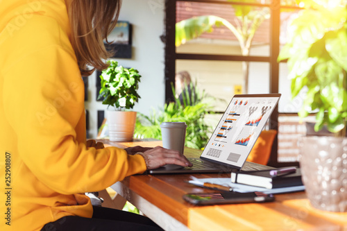 Close-up view of laptop screen with graphs,diagrams on monitor.Girl in yellow hoodie works on computer in cafe.Marketing