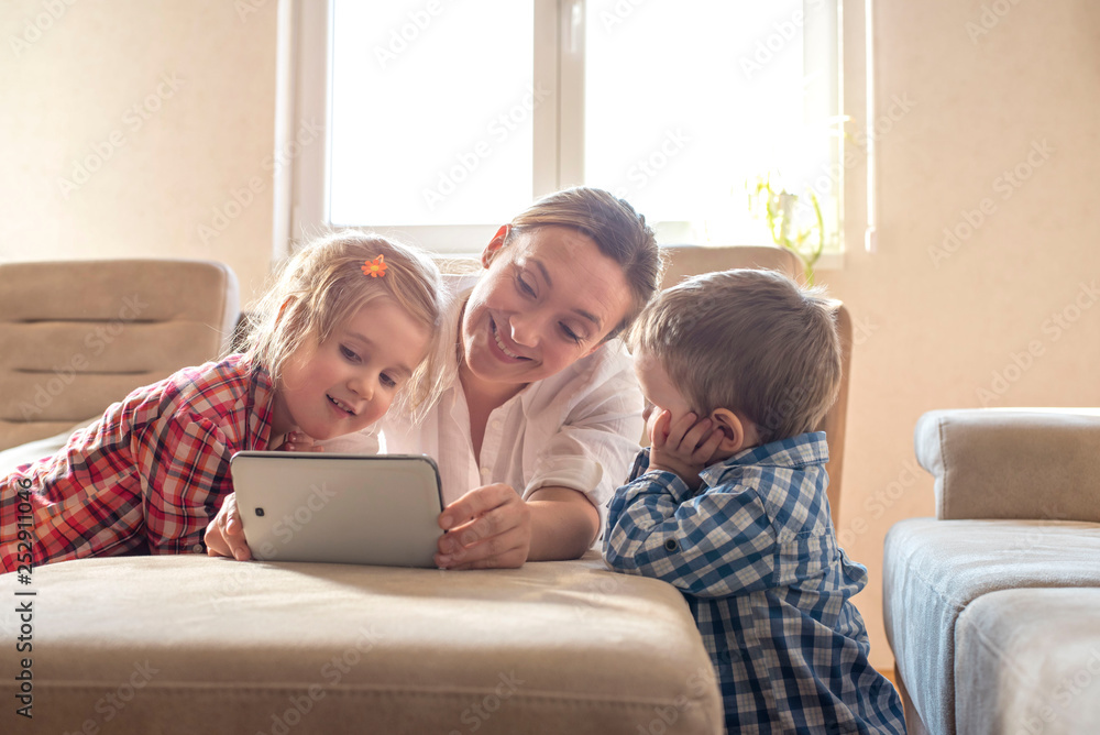 Mother with children watching cartoons on tablet and having fun together at home Mother with children watching cartoons on tablet and having fun together at home