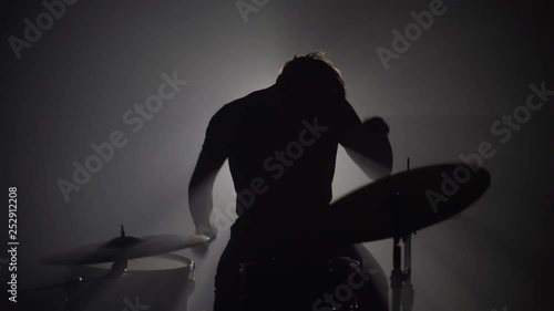 Silhouette of male drummer playing drums in dark photo
