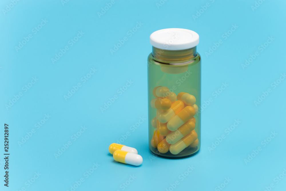 White and yellow pills, tablets and brown glass bottle on blue background White and yellow pills, tablets and brown glass bottle on blue background