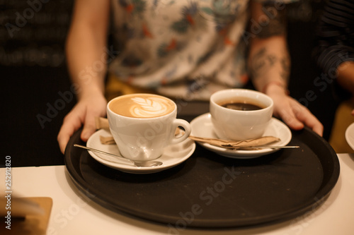 Woman bring two white cups of latte and americano coffe on tray