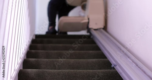 Senior Woman Sitting On Stair Lift At Home To Help Mobility