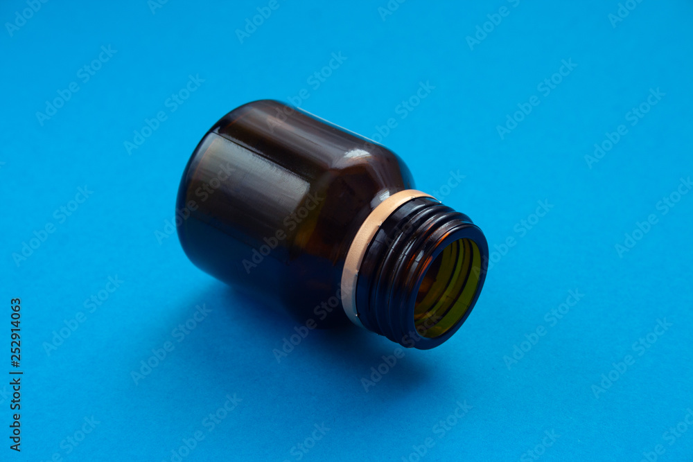 Empty glass dark bottle without pills on blue background. Medicines deficit concept. Empty glass dark bottle without pills on blue background. Medicines deficit concept.
