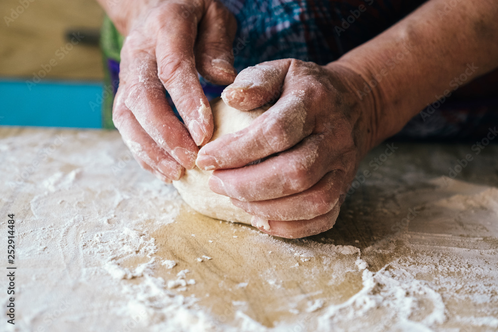 Wrinkled hands of older woman kneading dough