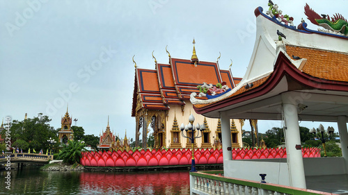 Asian style buddhist temple standing on the lake. Multi colored buildings and a bridge leading inside.