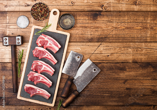 Fresh raw butchers lamb beef cutlets on chopping board with vintage meat hatchets and hammer on wooden background.Salt, pepper and oil. Space for text