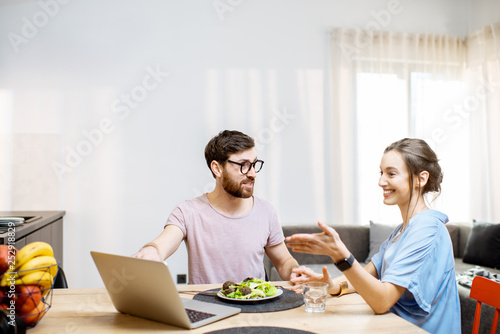 Young couple using laptop during the dinning time with healthy salad in the living room of the modern apartment