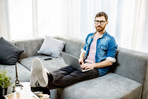 Man working with laptop on the couch at the bright living room of the modern apartment