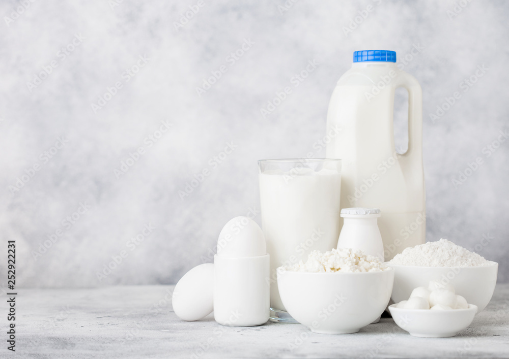 Fresh dairy products on white table background. Plastic bottle and glass of milk, bowl of cottage cheese and baking flour and mozzarella. Eggs and cheese. Space for text Fresh dairy products on white table background. Plastic bottle and glass of milk, bowl of cottage cheese and baking flour and mozzarella. Eggs and cheese. Space for text