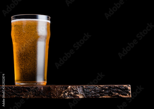 фотография Glass of lager beer with foam and bubbles on vintage wooden board on black background