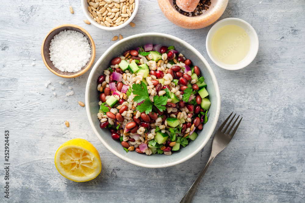 Healthy pearl barley salad with beans, cucumbers, red onion, sunflower seeds, pomegranate and parsley in bowl on concrete background. Top view. Healthy pearl barley salad with beans, cucumbers, red onion, sunflower seeds, pomegranate and parsley in bowl on concrete background. Top view.