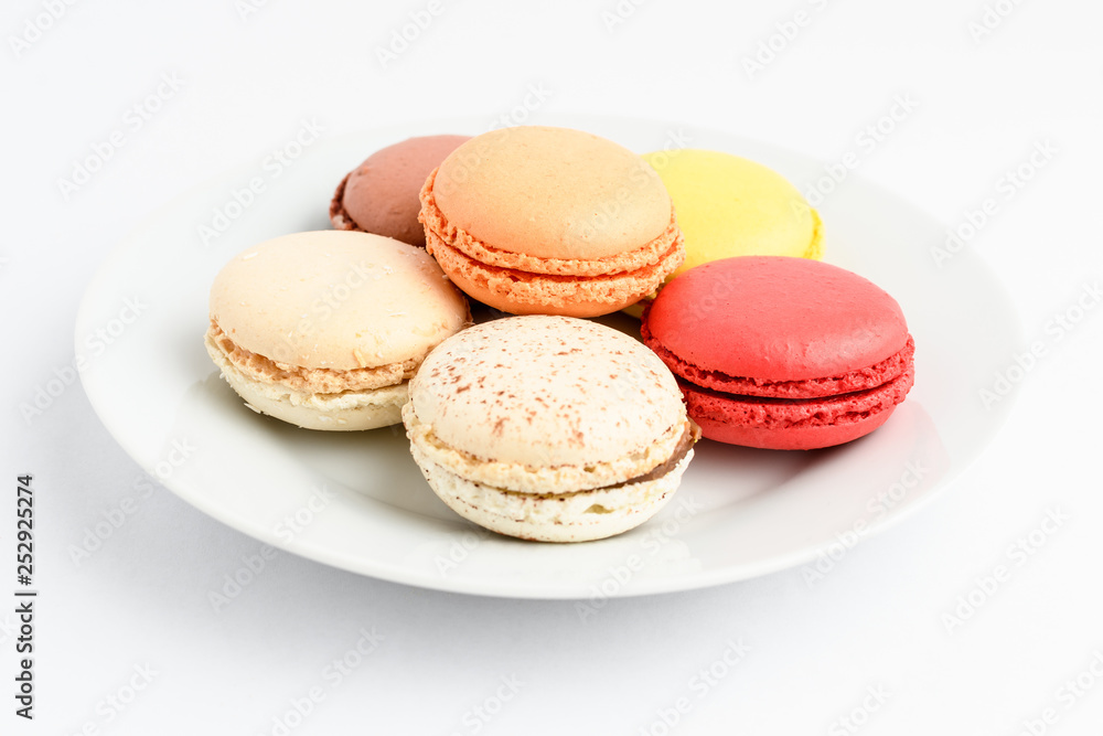 Group of six sweet French macarons on a white plate, isolated on white, flavours of strawberries,  lemon, caramel, vanilla, coconut and chocolate,  pastel colors