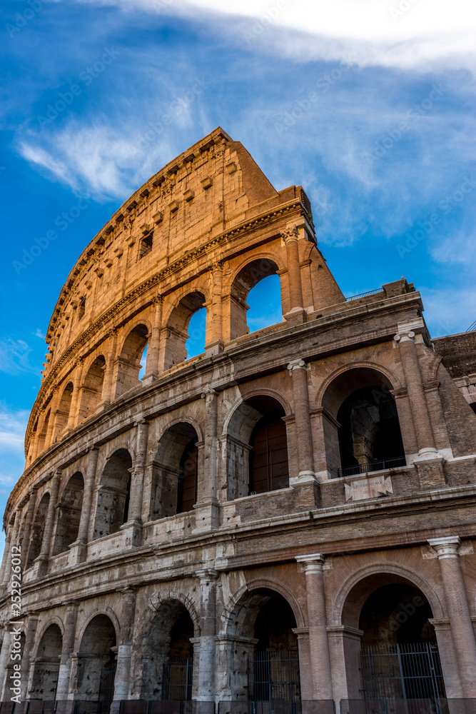 Fototapeta premium Golden sunset at the Great Roman Colosseum (Coliseum, Colosseo), also known as the Flavian Amphitheatre. Famous world landmark. Scenic urban landscape.