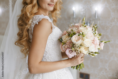 Beautiful young blonde bride with stylish wedding hairstyle in a white fashionable dress with a bouquet of flowers in her hands