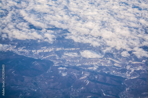 View from a plane window on clouds and blue clear sky and the earth from height. Beautiful view from air of mountains. 