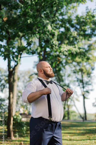 Stylish bearded fat groom in the park.