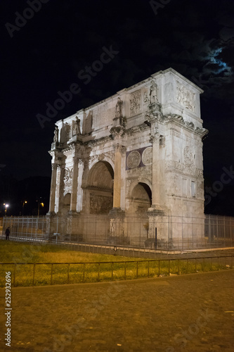 arch of constantine of the roman forum viewed through the gated arch of the passage at the entrance of the Roman Colosseum at night.