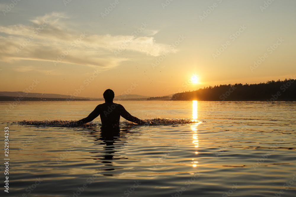 Silhouette of a man at sunset background. The guy on the waist plunged into the sea. Splashes water by hand.