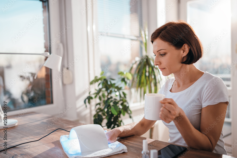 Woman drinking coffee while drying nails Woman drinking coffee while drying nails