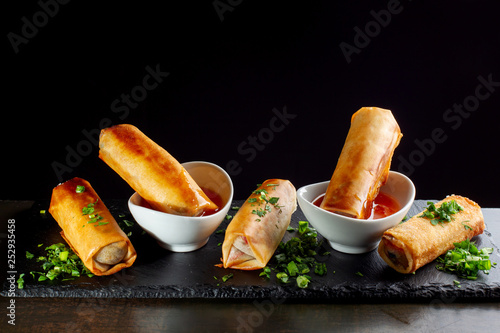 Фотография Fried spring rolls on black slate decorated with greens.
