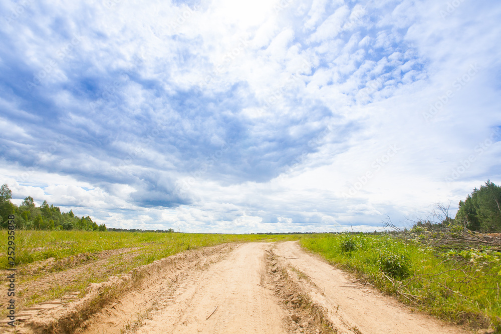 Spring summer background - rural road in green grass field meadow scenery lanscape with blue sky Spring summer background - rural road in green grass field meadow scenery lanscape with blue sky