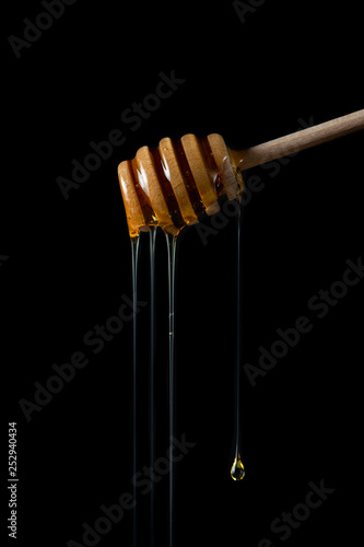 Honey dripping from dipper on isolated black background 