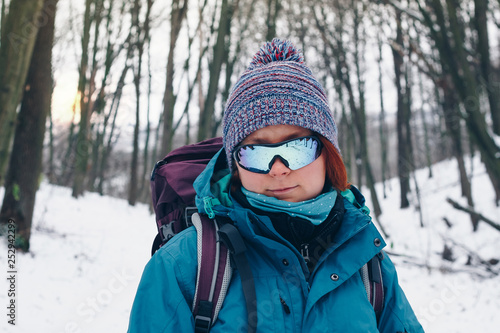 Young girl with backpack and sunglasses looks forward hiking through the winter forest