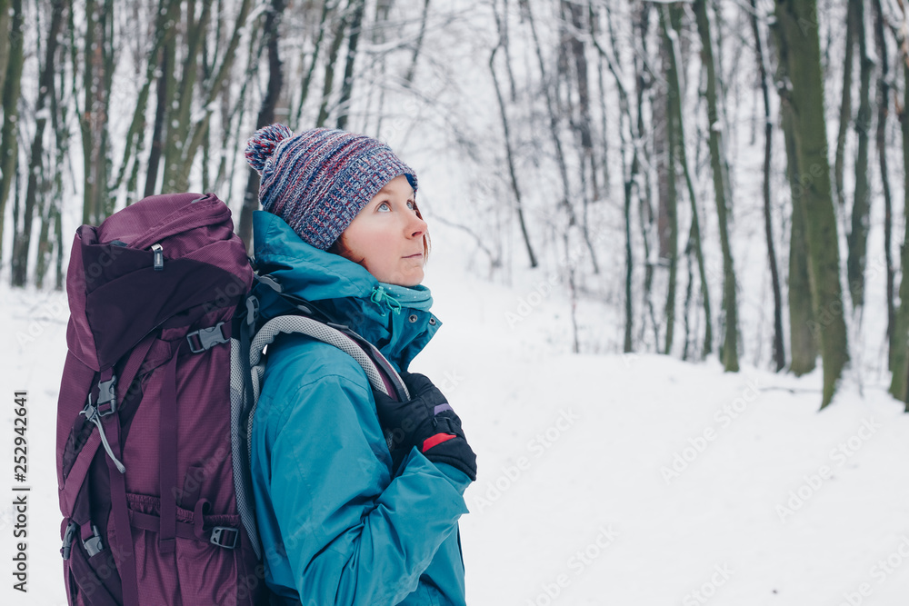 Young girl with backpack looks up staying in the winter forest. Look from the right side Young girl with backpack looks up staying in the winter forest. Look from the right side