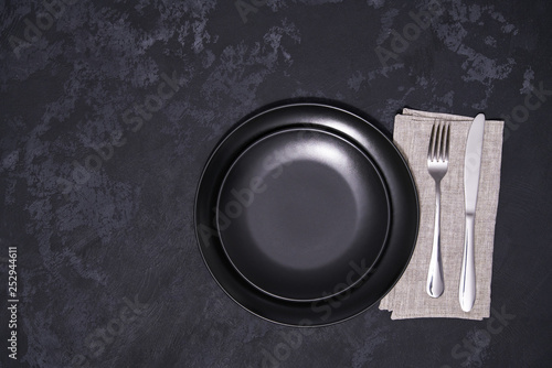 Two empty black plates and cutlery on a black background, top view.