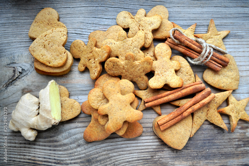 Gingerbread cookies in shapes of heart, star and man with cinnamon stick and ginger root on wooden table Gingerbread cookies in shapes of heart, star and man with cinnamon stick and ginger root on wooden table