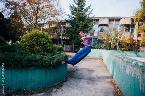 Young parkour guy jumping over a concrete wall and landing on another concrete wall while doing tricks in the air. © qunica.com