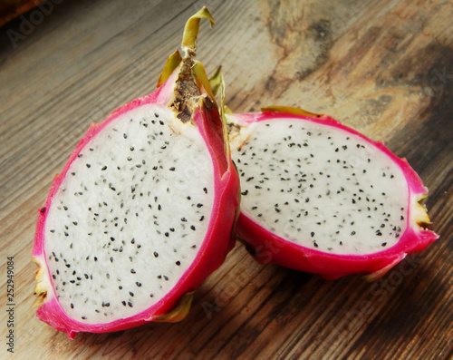 Juicy pink pitaya cut in two pieces on wooden table closeup