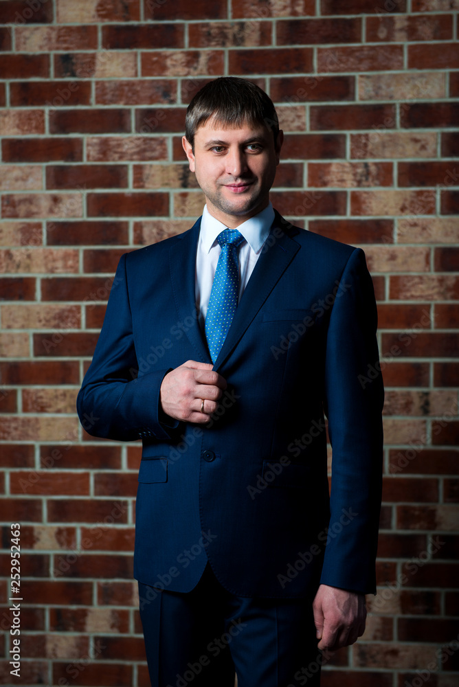 Serious male lawyer businessman in strict business suit and tie standing in the interior against the brown brick wall background Serious male lawyer businessman in strict business suit and tie standing in the interior against the brown brick wall background