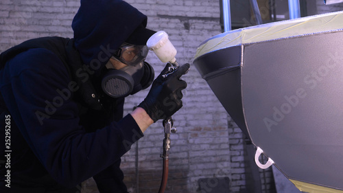 A professional guy (man) in the garage covers the yacht (transport) with a mini-jet (sprays) by applying paint (ceramics) to the surface using a protective suit dispenser and protective glasses. © dkHDvideo